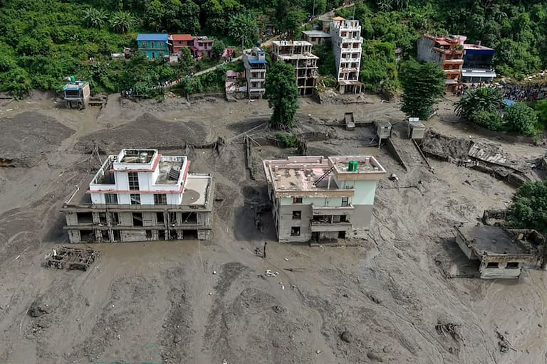 Houses lie partially submerged in muddy water along a riverside after flash floods at Trishuli Bazar in Nepal's Nuwakot district on August 26, 2026. A massive flood swept through Nepal's northern Rasuwa district on August 26, damaging roads and power infrastructure as authorities scrambled to assess the scale of the destruction. (Photo by Prabin RANABHAT / AFP)