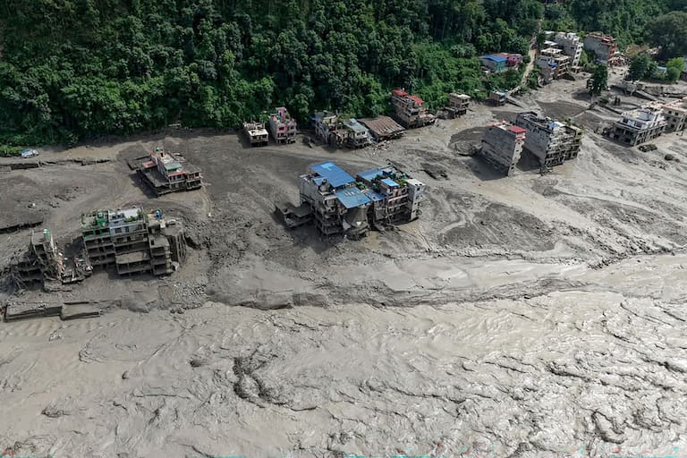 Houses lie partially submerged in muddy water along a riverside after flash floods at Trishuli Bazar in Nepal's Nuwakot district on August 26, 2026. A massive flood swept through Nepal's northern Rasuwa district on August 26, damaging roads and power infrastructure as authorities scrambled to assess the scale of the destruction. (Photo by Prabin RANABHAT / AFP)