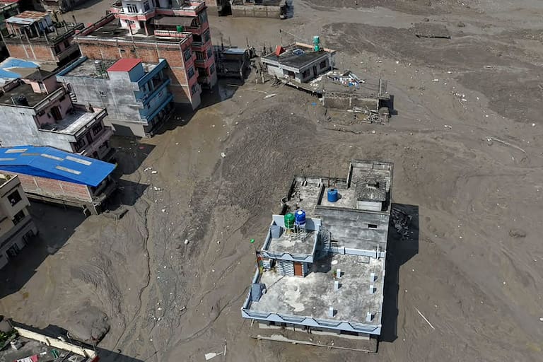 Houses lie partially submerged in muddy water along a riverside after flash floods at Trishuli Bazar in Nepal's Nuwakot district on August 26, 2026. A massive flood swept through Nepal's northern Rasuwa district on August 26, damaging roads and power infrastructure as authorities scrambled to assess the scale of the destruction. (Photo by Prabin RANABHAT / AFP)