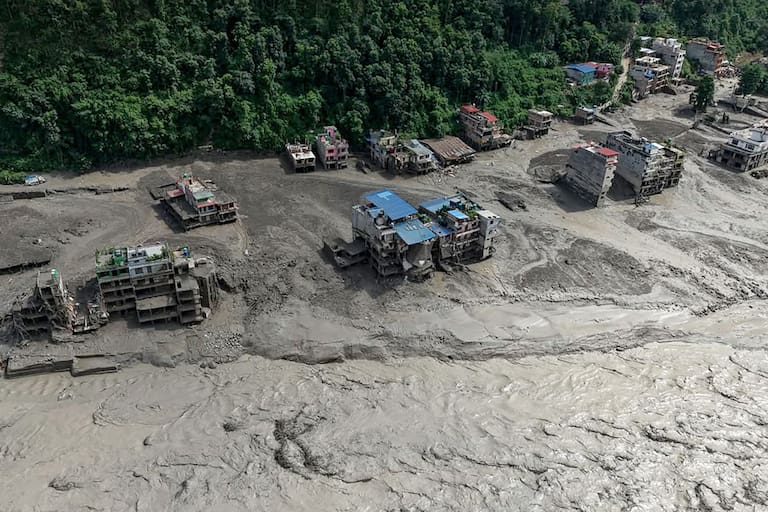 Houses lie partially submerged in muddy water along a riverside after flash floods at Trishuli Bazar in Nepal's Nuwakot district on August 26, 2026. A massive flood swept through Nepal's northern Rasuwa district on August 26, damaging roads and power infrastructure as authorities scrambled to assess the scale of the destruction. (Photo by Prabin RANABHAT / AFP)