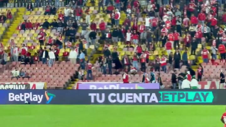 Uno de los registros muestra a hinchas corriendo por un pasillo de la tribuna mientras los jugadores esperaban en el campo de juego