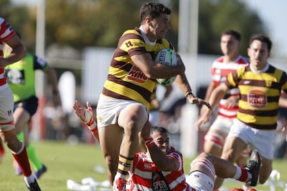 Ignacio Díaz, de Belgrano, intenta progresar con la pelota; lo tacklea Ramón Fuentes, de Alumni