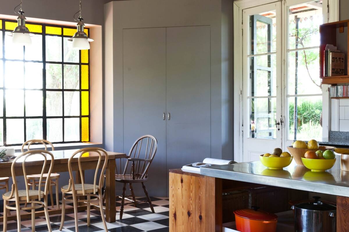 Igual que en living, el ventanal del comedor tiene vidrio repartido con guarda amarilla que suaviza la entrada de luz. Mesa con base de cobre y tapa de mármol y una taza gigantesca que se usa como florero.