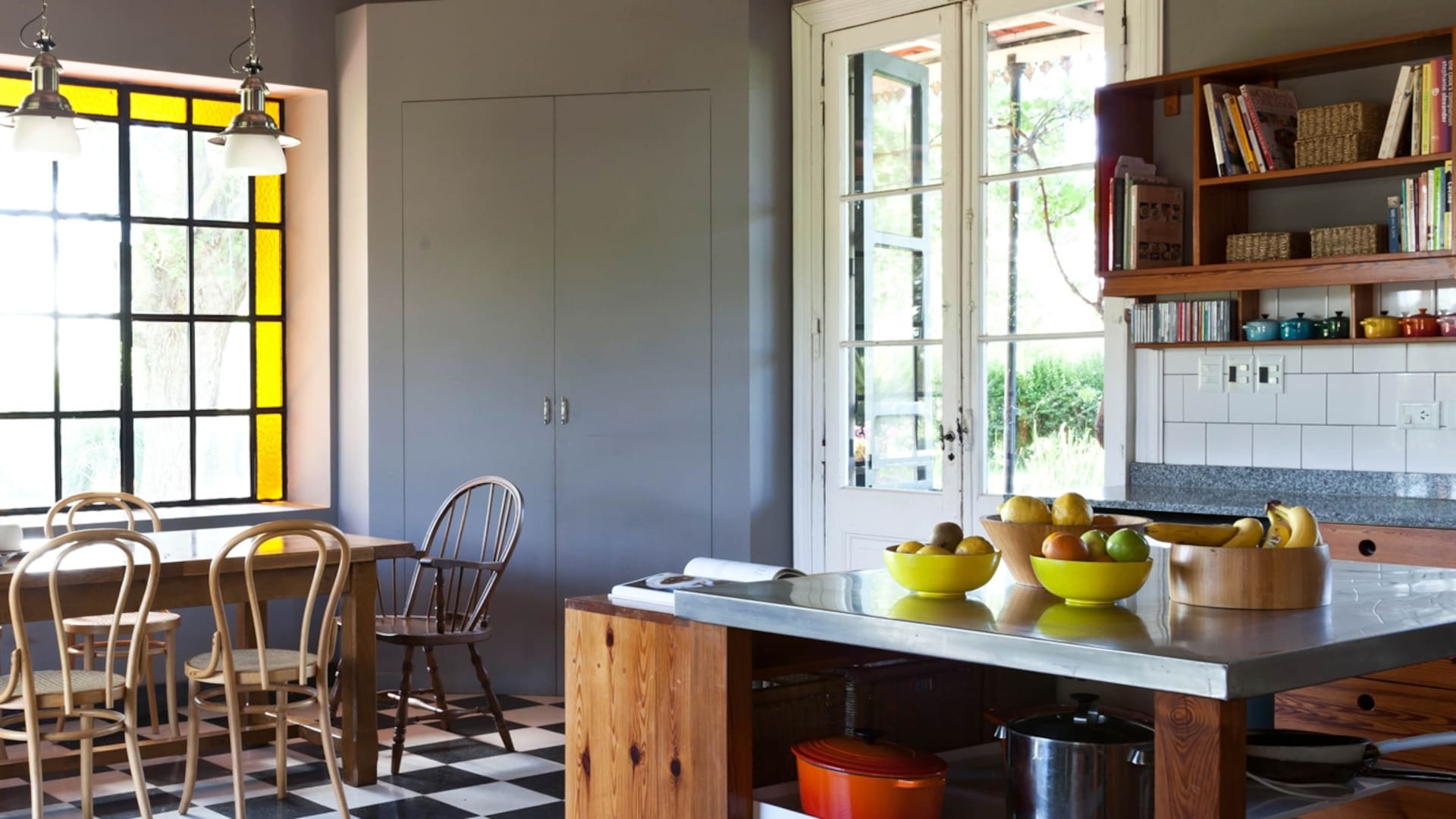 Igual que en living, el ventanal del comedor tiene vidrio repartido con guarda amarilla que suaviza la entrada de luz. Mesa con base de cobre y tapa de mármol y una taza gigantesca que se usa como florero.