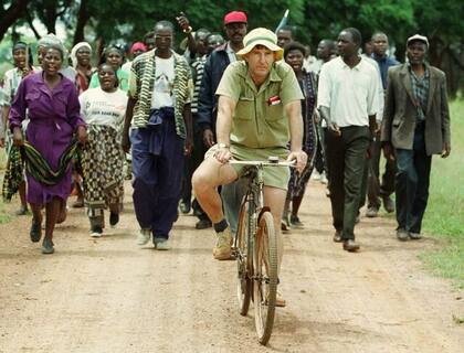 Imagen de 2019: el agricultor Tommy Bayley avanza en bicicleta seguido por veteranos de guerra y aldeanos que habían invadido su granja Danbury Park, en Zimbabue, durante el período de ocupaciones ilegales de tierras tras la derrota del gobierno en un referéndum constitucional