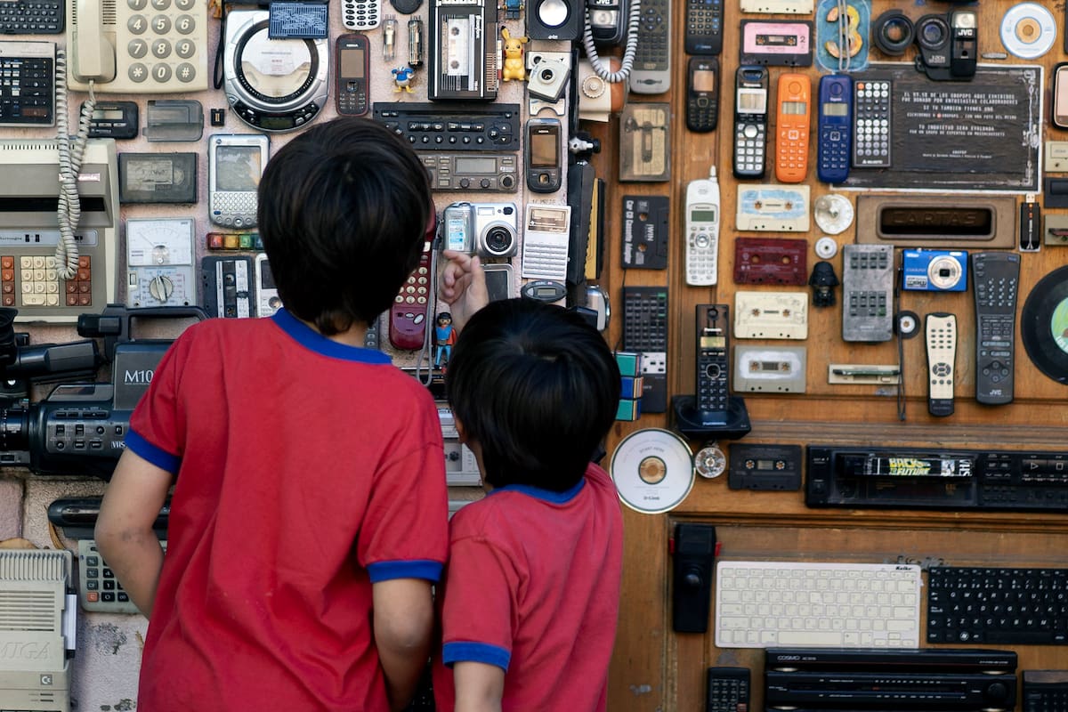 Imagen del 24 de abril de 2026 de niños observando la intervención urbana "Obopop", la cual se encuentra montada en la vereda de la casa del artista argentino, Lucas Stoessel, en la ciudad de Buenos Aires, capital de Argentina. Stoessel creó una obra de arte con objetos emblemáticos de los años 1980 y 1990 como "walkmans", teléfonos de disco, televisores, teclados y "joysticks", y la instaló en la puerta de su casa en Buenos Aires para deleite de los transeúntes. (Xinhua/Martín Zabala)