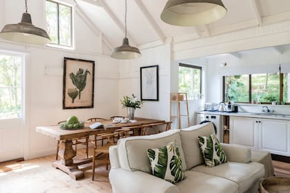 Imagen del living comedor de la cabaña, cuya sofisticada apariencia actual en blanco sobre blanco con toques botánicos es obra de la diseñadora de interiores australiana Kate Platt.