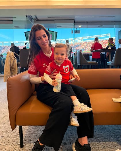 Iman (con camiseta, jogger y zapatillas Golden Goose) sonríe a cámara en brazos de su mamá, sin soltar la mamadera