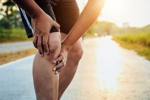 Injury from workout concept : The asian man use hands hold on his knee while running on road in the park. Shot in morning time, sunlight and warm effect with copy space for text or design