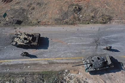 Insurgentes sirios montan en motocicleta entre tanques abandonados del Ejército sirio en una carretera a las afueras de Hama, Siria, el martes 3 de diciembre de 2024