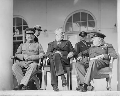Iósif Stalin, Franklin D. Roosevelt y Winston Churchill en la terraza de la legación soviética en Teherán, en noviembre de 1943, durante la primera Conferencia de los Tres Grandes. En la capital iraní los líderes de la Unión Soviética, Estados Unidos y el Reino Unido se reunieron por primera vez cara a cara para coordinar la estrategia militar contra la Alemania nazi y comenzar a trazar los primeros esbozos del nuevo orden mundial que emergería tras la guerra.