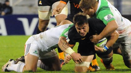 Isa al piso, tackleado por dos hombres de Highlanders; atrás, Cordero y Leguizamón