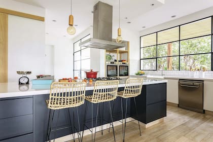 Isla central laqueada (HPS Design, Fabián Portal) con anafe y mesada de Silestone en ‘WhiteStorm’. Banquetas de mimbre (Brugués Mosconi).