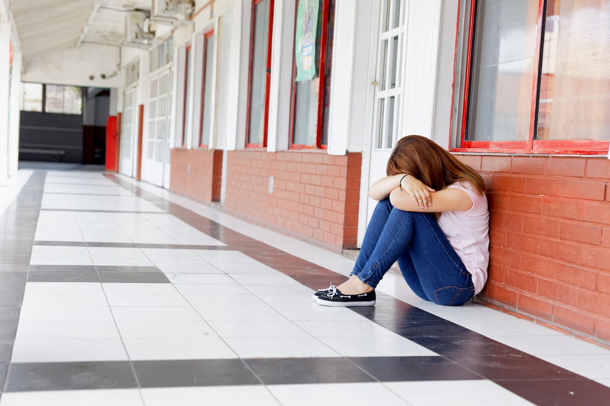 Isolated teenager girl seated desperate in the school hallway. Bullying concept.