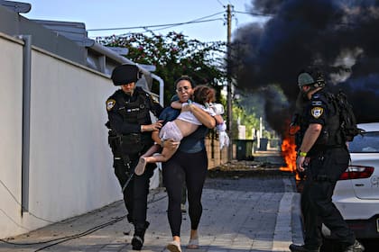 Agentes de policía israelíes evacuan a una mujer y un niño de un lugar alcanzado por un cohete lanzado desde la Franja de Gaza, en Ashkelon, sur de Israel, el sábado 7 de octubre de 2023