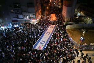 Israelíes marchan con una enorme bandera nacional durante una protesta contra los planes de reforma judicial propuestos por el gobierno del primer ministro Benjamin Netanyahu, en Tel Aviv, Israel, el sábado 18 de febrero de 2023