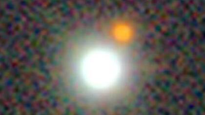 J0529-4351 es un disco brillante de materia alrededor de un agujero negro supermasivo y es 500 billones de veces más brillante que el Sol. (El punto naranja es una estrella vecina).