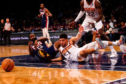 James Harden (13), de los Nets de Brooklyn, y Devin Booker (1), de los Suns de Phoenix, disputan el balón en el suelo en la segunda mitad del partido de la NBA, en Nueva York, el sábado 27 de noviembre de 2021. (AP Foto/Jessie Alcheh)