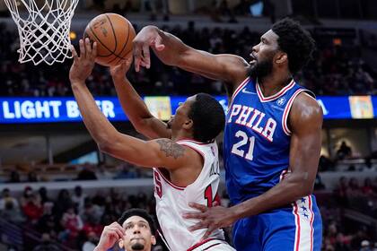 Joel Embiid, derecha, de los 76ers de Filadelfia, bloquea un tiro de Malcolm Hill, de los Bulls de Chicago, durante la segunda mitad del juego de la NBA, en Chicago, el domingo 6 de febrero de 2022. (AP Foto/Nam Y. Huh)