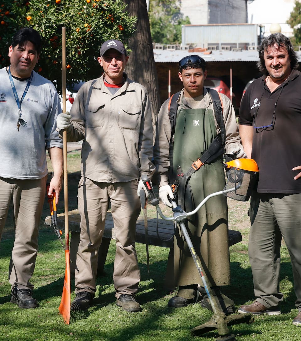 Jonathan y Ángel (en el centro), fueron limpiavidrios durante años y hoy trabajan en la empresa Kazaró, en el mantenimiento de espacios verdes. En la foto posan junto al encargado de su cuadrilla y su supervisor.