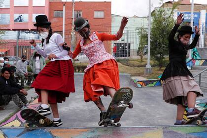 Milenda Limachi, Yanira Villarreal, y Aydé Choque, con barbijos y vestidas como cholas en sus patinetas