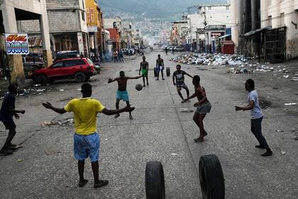 Jóvenes juegan al fútbol frente a comercios cerrados debido a una huega general en Puerto Príncipe, Haití, 18 de octubre de 2021. Trabajadores furiosos por la falta de seguridad declararon la huelga  general en protesta contra la falta de seguridad luego del secuestro de 17 misioneros estadounidenses por una pandilla violenta. (AP Foto/Matias Delacroix)