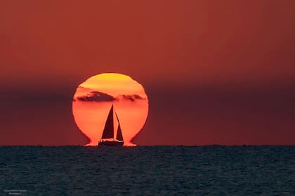 La imagen del fotógrafo español, Juan Antonio Sendra, muestra al sol con el denominado "efecto omega", que es una ilusión óptica en la que parece que la base del astro apoya sus "pies" sobre el mar justo por delante de un velero