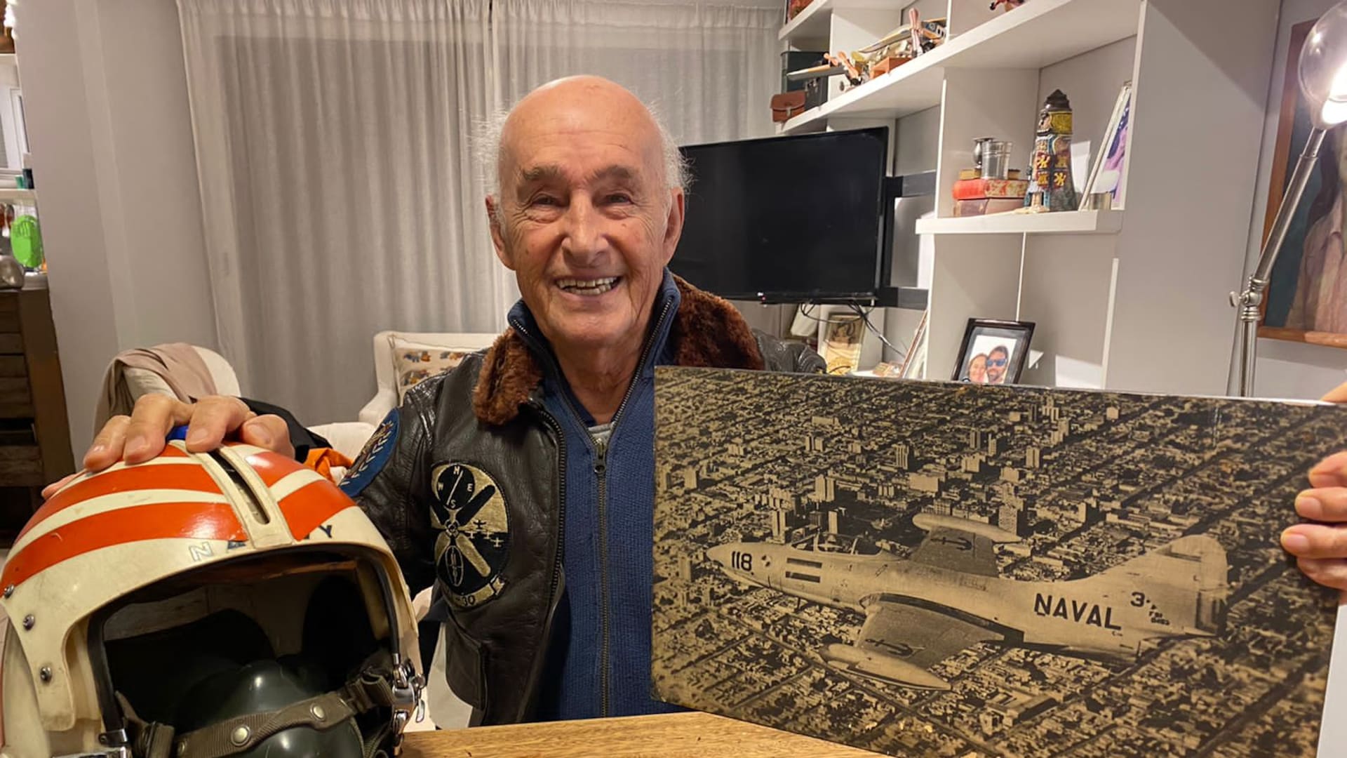 Juan Maria Pechar en su hogar junto a uno de sus cascos de aviador naval que utilizó durante su permanencia en la Aviación Naval Norteamericana, su campera de vuelo y una imagen muy especial. (Gentileza Federico Pechar).