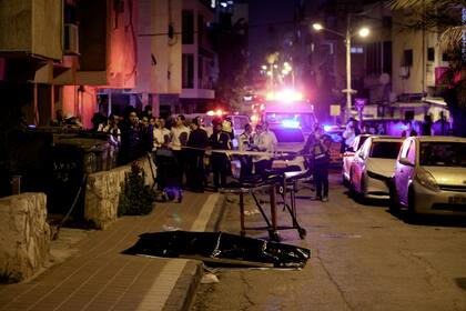 Judíos ultraortodoxos están cerca del cuerpo cubierto de una víctima del ataque en Bnei Brak, Israel, martes 29 de marzo de 2022. Un hombre en moto mató a cuatro personas. (AP Foto/Oded Balilty)