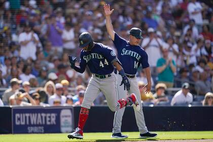 Julio Rodríguez, izquierda, de los Marineros de Seattle, reacciona con el coach de tercera base Manny Acta después de pegar jonrón de dos carreras durante la cuarta entrada del juego de béisbol en contra de los Padres de San Diego, el lunes 4 de julio de 2022. (AP Foto/Gregory Bull)