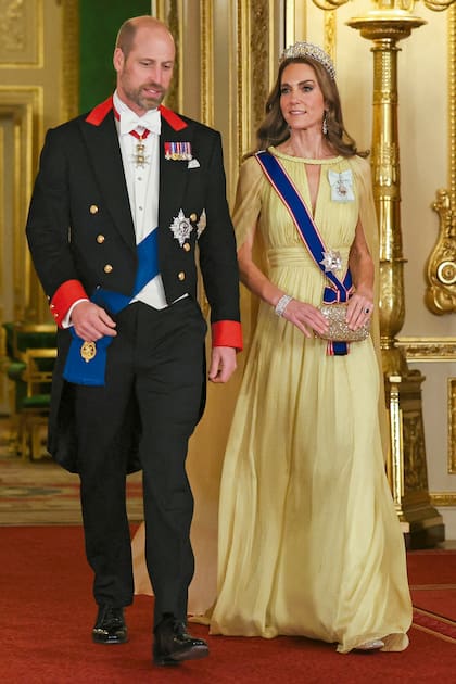 Kate impactó con un diseño de Elie Saab con silueta fluida, cintura marca y frunces. Lo acompañó con la tiara Cambridge Lover’s Knot –encargada por la reina María a la joyería Garrad en 1913–, pendientes de diamantes de Isabel II, brazalete de diamantes que perteneció a la reina María, clutch de Anya Hindmarch y stilettos Gianvito Rossi. Completó su estilismo con la banda y la estrella de la Real Orden Victoriana y la insignia de la Orden Familiar del rey Carlos III. A su lado, William, de white tie, llevó la Orden de la Jarretera con su estrella, una banda con la Orden de San Jorge Menor y varias medallas y condecoraciones