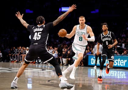 Kristaps Porzingis (8), de los Celtics de Boston, conduce hacia la canasta contra Keon Johnson (45) y Ziaire Williams (8), de los Nets de Brooklyn, durante la primera mitad de un partido de baloncesto de la NBA, el sábado 15 de marzo de 2025, en Nueva York. (AP Foto/Noah K. Murray)