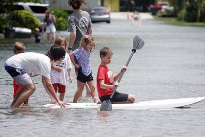 Kyle Hilderbrandt, a la derecha, rema sobre una calle inundada en Oakland Park, Florida, el sábado 4 de junio de 2022. La tormenta tropical Alex trajo fuertes lluvias e inundaciones al sur de Florida. (Joe Cavaretta/South Florida Sun-Sentinel via AP)
