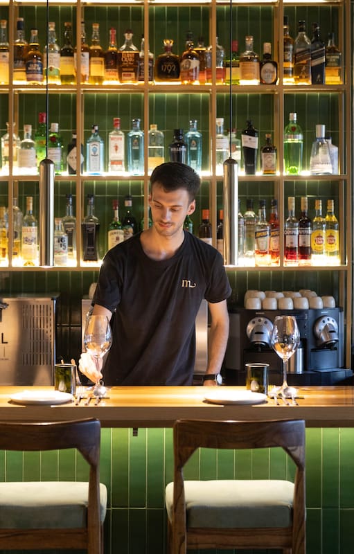 La barra y cocina a la vista, con predominio de madera y tonos verdes, plantas y una cantidad de luz justa para quienes van a la noche.