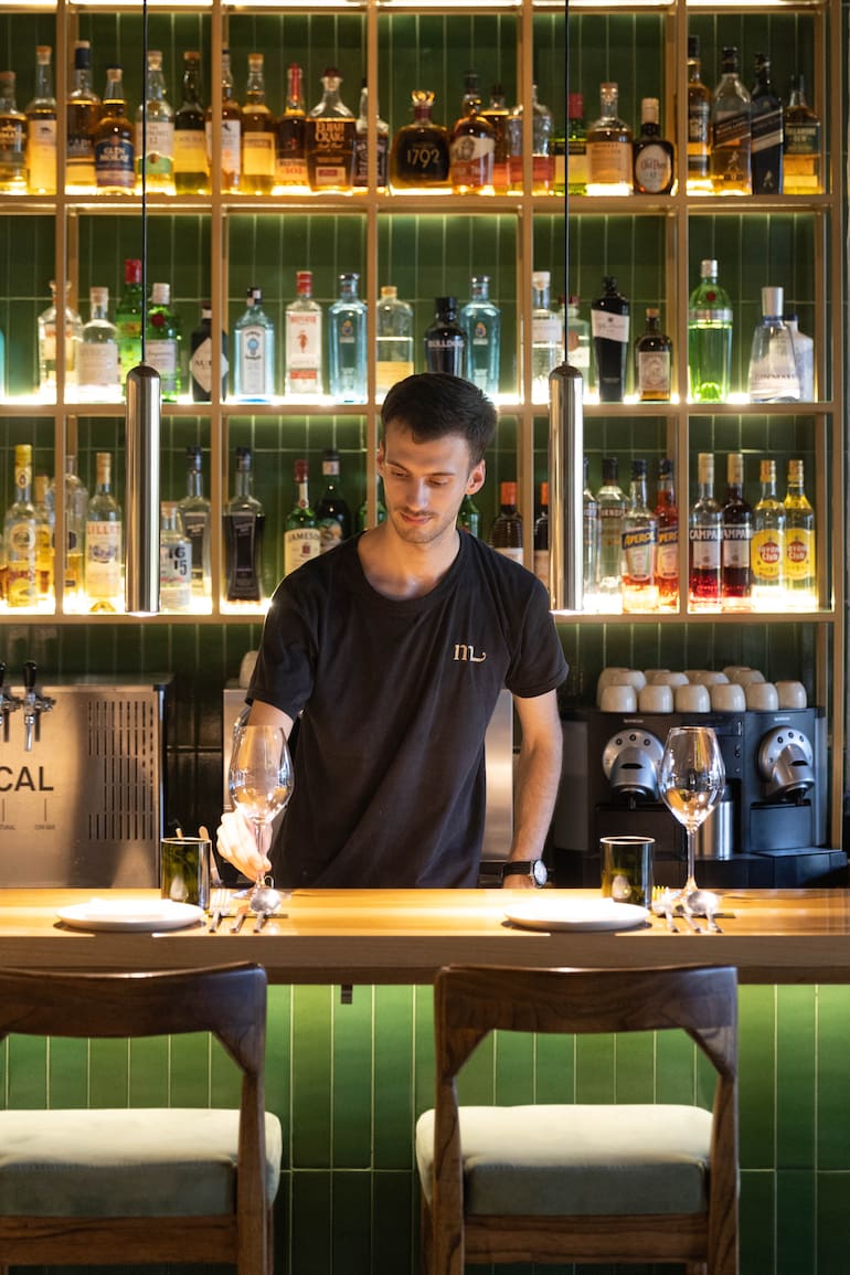 La barra y cocina a la vista, con predominio de madera y tonos verdes, plantas y una cantidad de luz justa para quienes van a la noche.