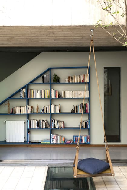 La biblioteca a medida (Monoestudio) repite la forma trapezoidal del muro de la escalera, regala color desde el marco y el contenido al patio y aprovecha el pasillo que conecta toda la planta baja.