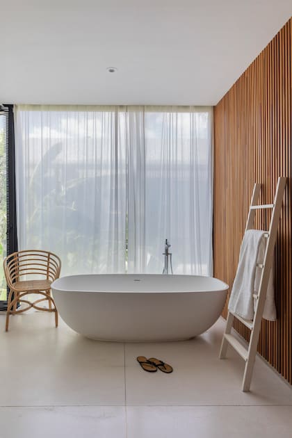 La caja de Neolith se matiza con las cortinas de gasa y el revestimiento de madera natural de tauarí (Indusparquet). Bañadera exenta con grifería de pie (Hansgrohe).