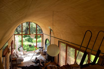 La casa cuenta con dos niveles, una planta baja abierta y luminosa que alberga la cocina abierta al comedor, el baño y el dormitorio principal, distribuidos en torno a un volumen central de madera y una planta alta que se accede mediante una escalera de hierro con ruedas que permite plegarse para ganar más espacio.