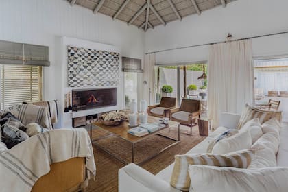 La chimenea preside el living coronada por las boyas tramadas de la artista Marina Marré. En torno a la mesa ratona, un sillón francés tapizado en arpillera y cubierto con un lino antiguo (Linos Vintage), sofá y dos sillones individuales en gamuza color arena.