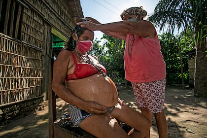 La comadrona Paje Suzete de la tribu Kumaruara baña a su hija embarazada antes del parto de su bebé en su casa junto al río Tapajos del municipio de Santarem en el oeste del estado de Pará, Brasil, el 10 de julio de 2020, en medio de la pandemia de coronavirus