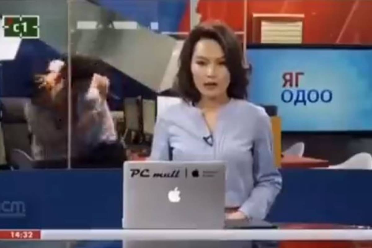 La conductora presenta una noticia mientras dos hombres, detrás de ella, se trenzan en una pelea, en un noticiero de Mongolia