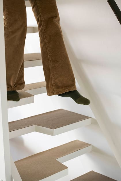 La escalera de pasos alternados, muy popular en España durante los 80, se modernizó con pintura blanca y alfombras en dos tonos de beige para diferenciar los peldaños.