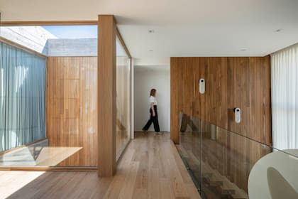 La escalera desemboca en este espacio de distribución con baranda vidriada (Pablo Sapia Arquitectura). Sobre la pared en madera, apliques ‘Eclipse’ de piedra (La Feliz).