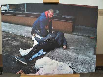 La fotografía de la exposición muestra un civil cargando a un cadáver por las calles de Bucha, Ucrania