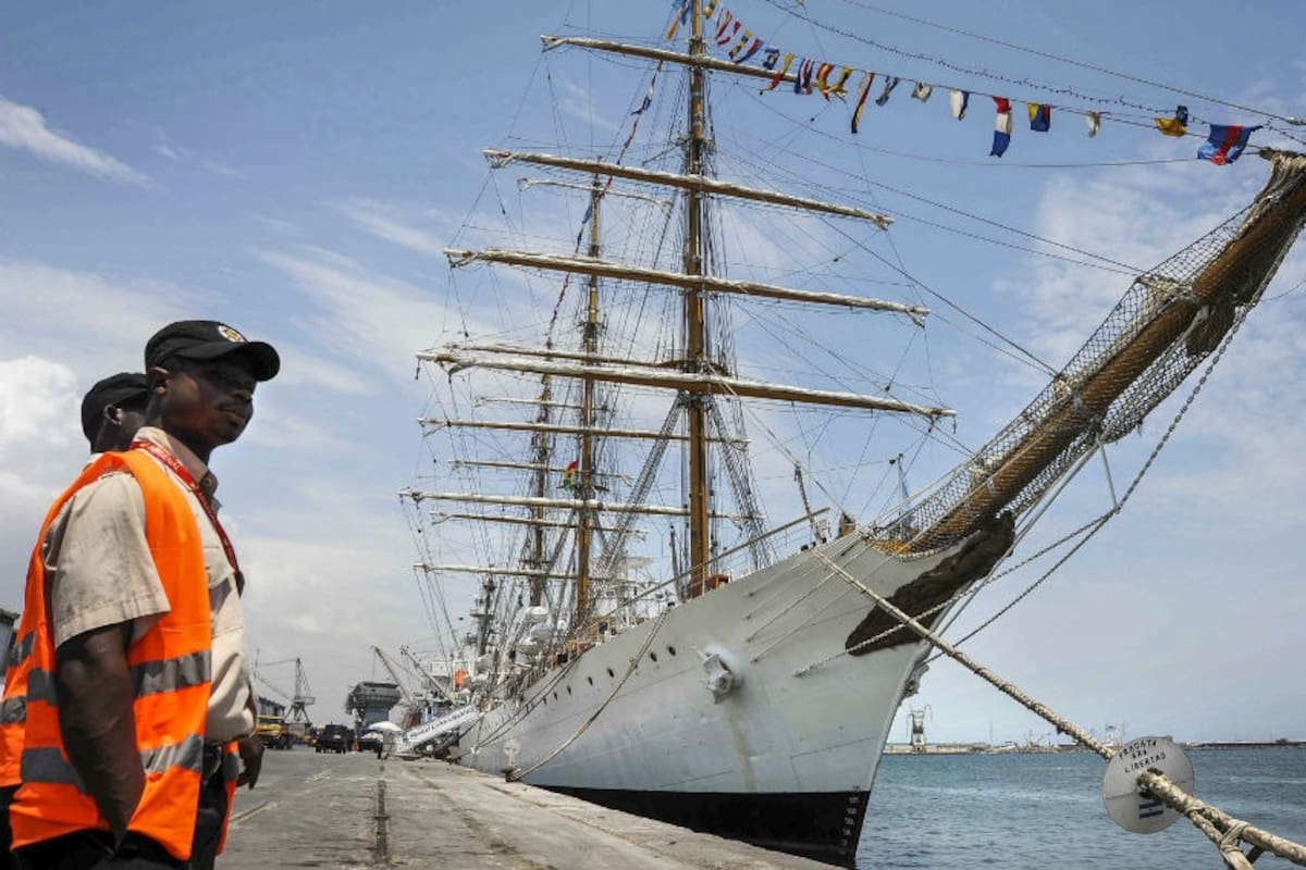 El buque escuela, en el puerto de Tema, cerca de Accra, la capital del país africano, con la bandera local. A la izquierda, dos funcionarios locales que trabajaban en el muelle.