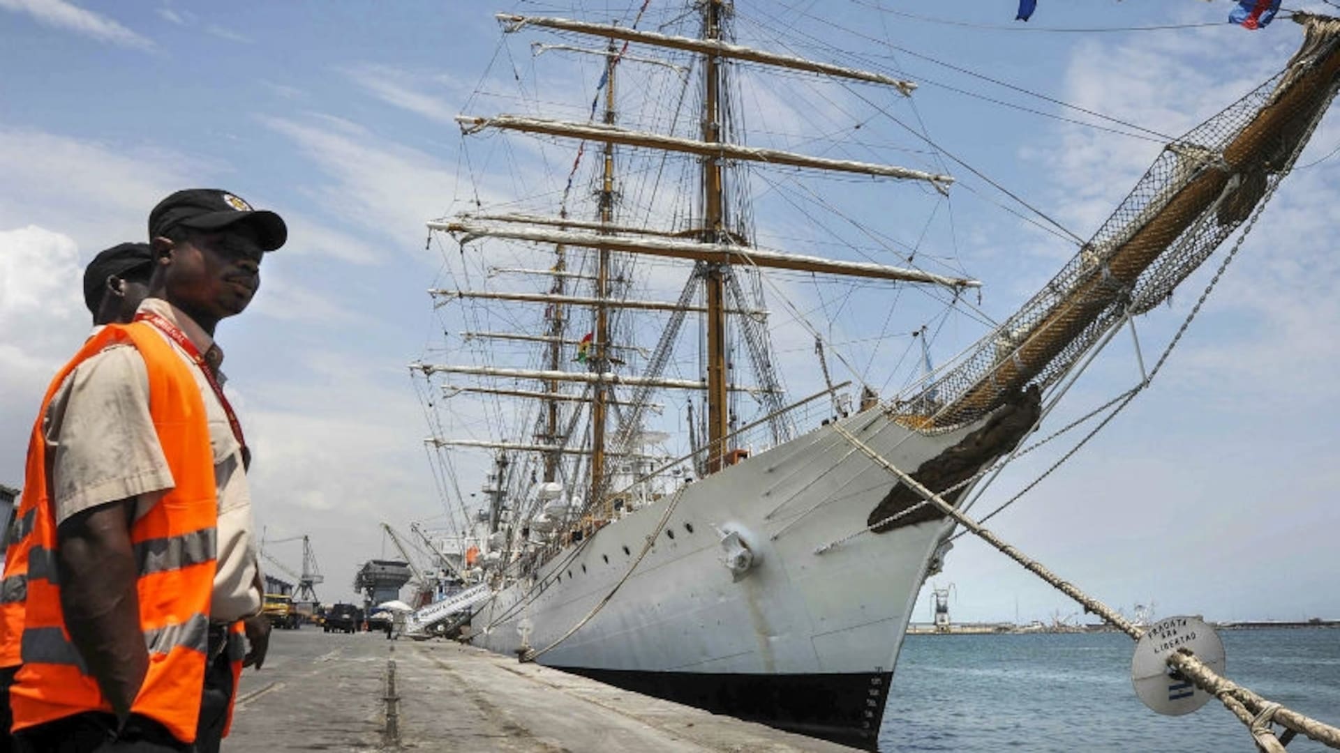 El buque escuela, en el puerto de Tema, cerca de Accra, la capital del país africano, con la bandera local. A la izquierda, dos funcionarios locales que trabajaban en el muelle.