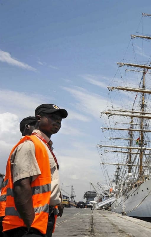 El buque escuela, en el puerto de Tema, cerca de Accra, la capital del país africano, con la bandera local. A la izquierda, dos funcionarios locales que trabajaban en el muelle.