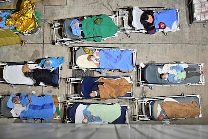 La gente duerme en camas de hospital con temperaturas que bajan durante la noche fuera del Centro Médico Caritas en Hong Kong, el 16 de febrero de 2022, mientras los hospitales se abruman con la ciudad que enfrenta su peor ola de coronavirus Covid-19 hasta la fecha. (Photo by Peter PARKS / AFP)