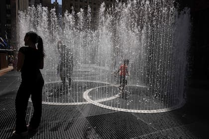 La gente juega en la escultura acuática del artista Jeppe Hein titulada "Changing Spaces" en el Rockefeller Center Plaza de Nueva York el 19 de julio de 2022, mientras continúa la ola de calor en Europa y Norteamérica.