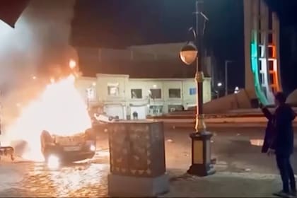 La imagen, tomada de un video distribuido el 9 de enero de 2026 por la televisora estatal iraní, muestra a un hombre sosteniendo un dispositivo para documentar la quema de vehículos durante una noche de protestas masivas en Zanjan, Irán